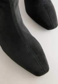 Bottines en daim noir avec un bout pointu, dotées de coutures bleu contrastantes le long des coutures pour ajouter une touche de détail.
