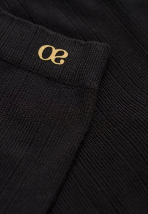 Schwarzer, gerippter Stoff mit einem sichtbaren, elastischen Taillenbund, der ein goldenes "30"-Logo trägt. Nahaufnahme, die Textur und Musterdetails hervorhebt.