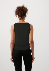 Top de tirantes acanalado de color verde oscuro con un diseño ajustado, corte sin mangas y escote redondeado, combinado con unos jeans negros.