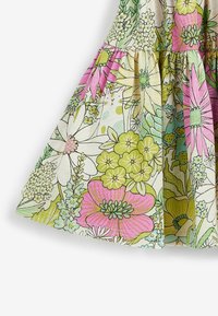 Květinové šaty vyrobené z bavlněné látky s vzory v zelené, růžové a žluté barvě, se sklady blízko lemování a lehkou texturou.