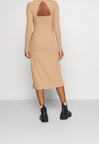 Abito beige a maniche lunghe con taglio sulla schiena, design aderente, lunghezza midi e texture liscia, abbinato a stivaletti neri chunky alla caviglia.