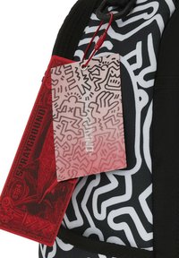 Mochila con un patrón en blanco y negro, con un tejido suave y una etiqueta roja texturizada que presenta un diseño gráfico y un logotipo.