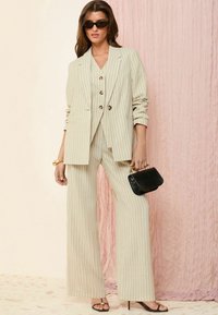 Set de costum bej cu dungi subțiri, format dintr-un sacou ajustat și pantaloni cu picioare largi. Complementat de o geantă mică neagră și tocuri cu bandă.