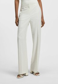 Gestreepte wijde broek in lichtcrème met subtiele verticale lijnen. Gemaakt van een gladde stof met een hoge tailleband. Gecombineerd met sandalen met blokhak en bandjes.