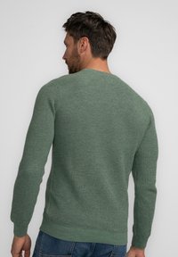 Maglione verde lavorato a maglia con motivo testurizzato, maniche lunghe e scollatura rotonda. L'orlo inferiore e i polsini sono a coste.