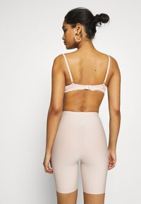 Lichtroze beha met kantdetails en verstelbare bandjes, gecombineerd met huidkleurige, aansluitende fietsshorts die tot halverwege de dij komen.