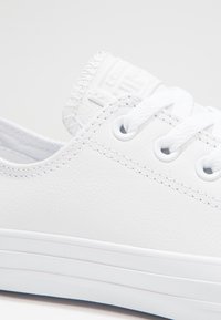 Sneaker bianco realizzato in pelle sintetica liscia, con lacci bianchi, fori per lacci e una linguetta sul tallone texturizzata con logo.