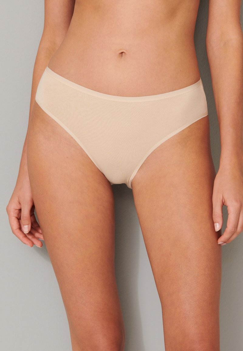 Slip in beige senza cuciture con una texture liscia e vita regolare, dotato di una semplice cintura elastica e un design minimalista.