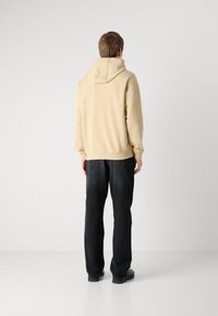 Sudadera beige con capucha ajustable, corte relajado, puños acanalados, combinada con pantalones de mezclilla oscuros y zapatos negros. Diseño simple y funcional.