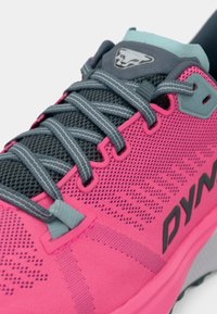 Ροζ αθλητικά παπούτσια που διαθέτουν αναπνεύσιμο πλέγμα στην πάνω μεριά, γκρι κορδόνια και μαυρο branding. Σημαντικές γκρι λεπτομέρειες προσθέτουν αντίθεση στο σχέδιο.