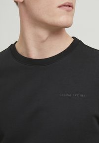 Fekete crewneck pulóver puha anyagból, az elülső részén diszkrét "CASUAL FRIDAY" logóval sötét nyomattal. Egyszerű, minimalista dizájn.