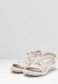 Beige gewebte Sandalen mit offenem Zehenbereich, Kreuzband-Design, verstellbarem Riemen am Hinterteil und strukturiertem Gummisohle.