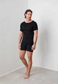 Black fitted t-shirt with short sleeves paired with black compression shorts. Worn by a male model, featuring a smooth, stretchy texture.