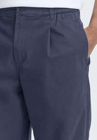 Navy blue trousers made of lightweight fabric, featuring an elastic waistband, front pleats, and side pockets for practical use.
