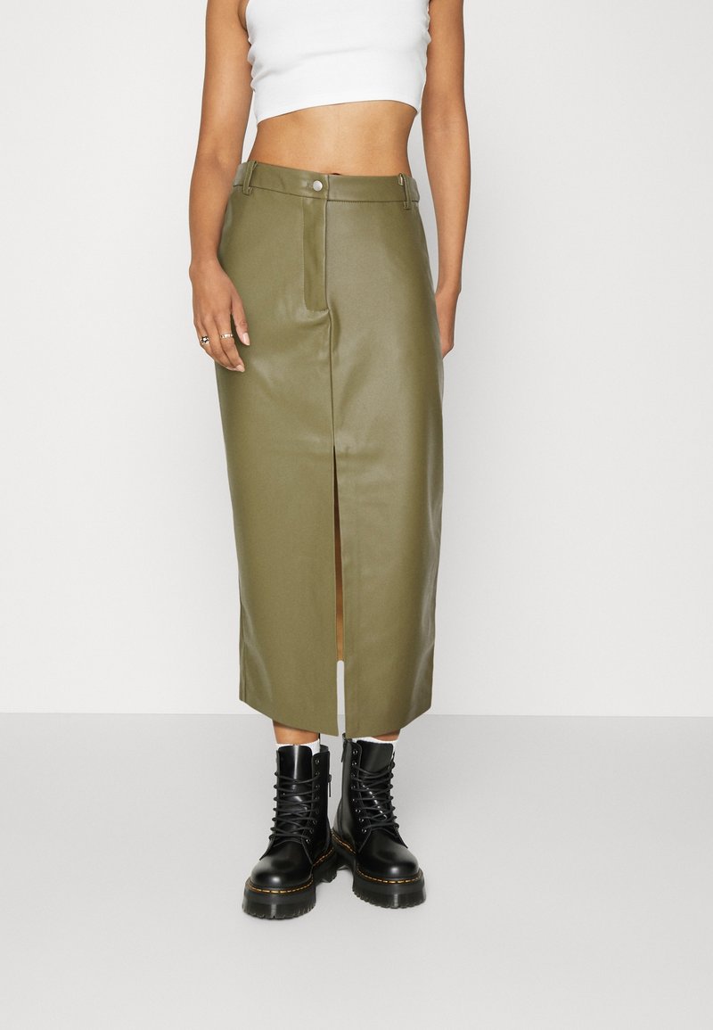 Jupe midi en simili cuir vert olive avec une fente à l'avant, taille haute et fermeture à boutons, associée à des bottes noires à lacets.
