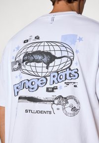 Hvit bomulls t-skjorte med svart grafikk av en rotte, globus, og teksten "Fringe Rats" med blå aksenter og stjerner.