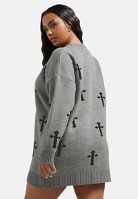 Grå stickad klänning med avslappnad passform, ribbad nederkant och svarta korsmönster spridda över tyget.