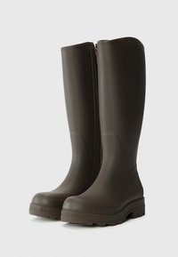 Bottes en caoutchouc marron jusqu'au genou avec une finition lisse, dotées d'une fermeture éclair sur le côté et d'une semelle à tread texturé pour une meilleure adhérence.