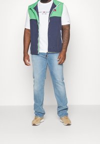 Marineblauer und grün blockierter Weste mit Reißverschluss, getragen über einem weißen T-Shirt und hellblauen Jeans, kombiniert mit beigen Sneakers.