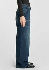 Jeans en denim à jambes larges de couleur bleu foncé, avec une taille haute, un design à cinq poches, et un léger délavage sur les cuisses. Texture lisse.