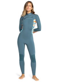 Wetsuit in teal neoprene with colorful zigzag patterns on the sides. Features a high neckline and seamless design for flexibility.