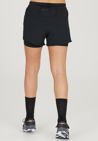 Zwarte sportshorts met een elastische tailleband en binnenvoering, gecombineerd met kniehoge zwarte sokken en donkere hardloopschoenen.