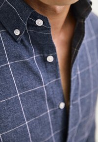 Navyblau kariertes Hemd aus strukturiertem Stoff mit weißen Gitterlinien und kontrastierenden weißen Knöpfen am Kragen.