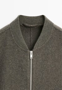 Giubbotto bomber in lana grigia con colletto a costine e chiusura frontale con zip. Texture morbida e design minimale.