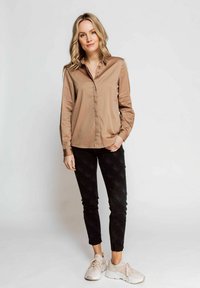 Light brown long-sleeve shirt with a button-down collar, paired with black textured pants and light sneakers, featuring a casual fit.