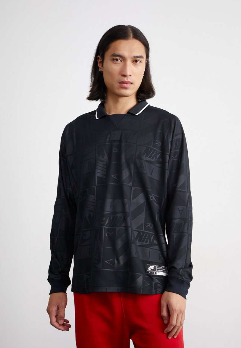 Camisola preta de mangas longas com padrões geométricos, detalhe de colarinho branco e um pequeno emblema da Nike, feita de um tecido suave e leve.