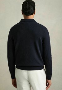 Tmavě modrý pletený svetr s žebrovaným límcem a manžetami, s texturovaným povrchem a volným střihem, zobrazený zezadu.