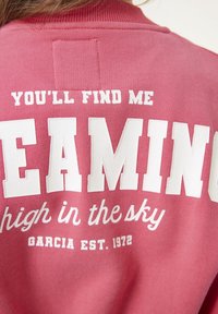 Retro di una felpa rosa con testo bianco: "Mi troverai a sognare in alto nel cielo. Garcia Est. 1972".