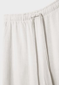 Pantalon en lin beige clair avec une taille élastique et un cordon de serrage noué visible sur le côté droit.