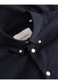 Camicia blu navy con bottoni realizzata in tessuto morbido, dotata di colletto classico e bottoni bianchi. Presenta un'etichetta con la scritta "LES DEUX" cucita sopra.