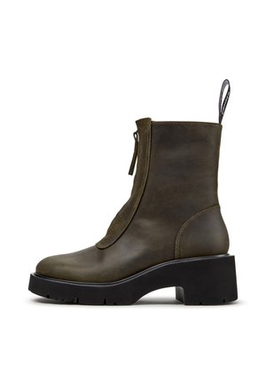 Olivgrüner Ankle Boot mit seitlichem Reißverschluss, dicker schwarzer Plateausohle, abgerundeter Spitze und Zuglasche hinten vor weißem Hintergrund.