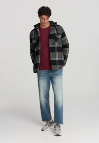 Czarna i szara w kratę flanelowa koszula z kapturem, zestawiona z bordowym podkoszulkiem i jasnoniebieskimi luźnymi dżinsami. Srebrne buty sportowe.