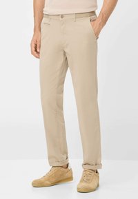 Beige Chinos mit schlanker Passform, mit einem Knopfverschluss, zwei Seitentaschen und leicht umgekrempelten Bündchen. Kombiniert mit tanfarbenen Wildledersneakern.