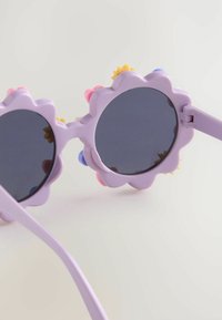 Lunettes de soleil rondes avec une monture lilas ornée d'un motif floral. Décorées d'accents roses, jaunes et bleus, avec des verres teintés foncés.