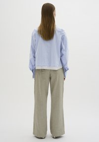 Camicia oversized a righe blu chiaro con maniche lunghe, indossata con pantaloni grigi a gamba larga e texture, caratterizzati da righe verticali.