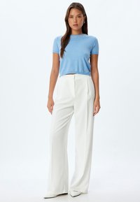 Top corto in maglia blu chiaro con maniche corte, adornato da un collo impreziosito da perline; abbinato a pantaloni bianchi a vita alta e gamba ampia.
