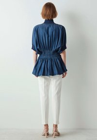 Denim peplum-topp med korta, puffiga ärmar och en ribbad krage, i kombination med vita skräddarsydda byxor och beige klackar med remmar.