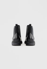 Botas de tobillo negras con un exterior de cuero liso, paneles laterales elásticos y una suela de goma texturizada con tiradores en la parte posterior.
