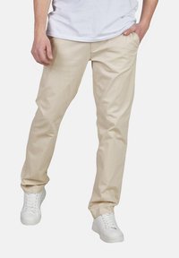 Beige Chino-Hosen mit geradem Bein, gefertigt aus Baumwollmischgewebe; kombiniert mit weißen Sneakers für einen lässigen Look.