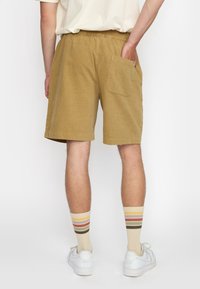 Khaki korte broek met een elastische tailleband, achterzak en een geweven stof. Gecombineerd met crèmekleurige sokken met meerkleurige strepen.