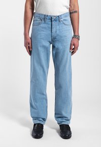 Jeans in denim blu chiaro con una vestibilità a gamba dritta, dotati di chiusura con bottone, tasche frontali e una texture leggermente sbiadita. Sono indossate scarpe nere.