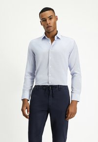 Camicia button-up azzurro chiaro con maniche lunghe, tessuto strutturato e colletto, abbinata a pantaloni con elastico in vita di un blu navy scuro.