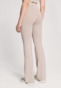 Jasnobeżowe, rozszerzane legginsy z miękkiego, elastycznego materiału; wysoki pas z logo; gładka faktura i dopasowany krój, w zestawie z trampkami.