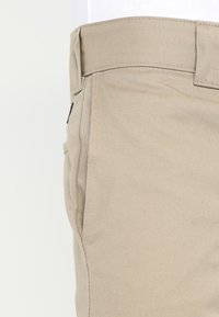 Béžové bavlněné kalhoty s texturovaným povrchem, rovného střihu a bočními kapsami. Pas je mírně zvýšený s jemným prošíváním.