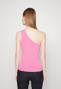 Asymmetrisches pinkes Tanktop aus gestricktem Stoff, mit einer freiliegenden Schulter und einer figurbetonten Silhouette, kombiniert mit dunklen Jeans.