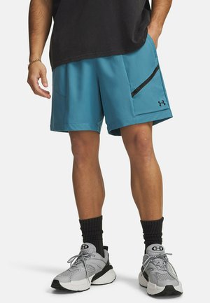 Turquoise sportshirts met een zwart ritssluitingvak, vlakke naden en een Under Armour-logo, gecombineerd met grijze sneakers en zwarte sokken.